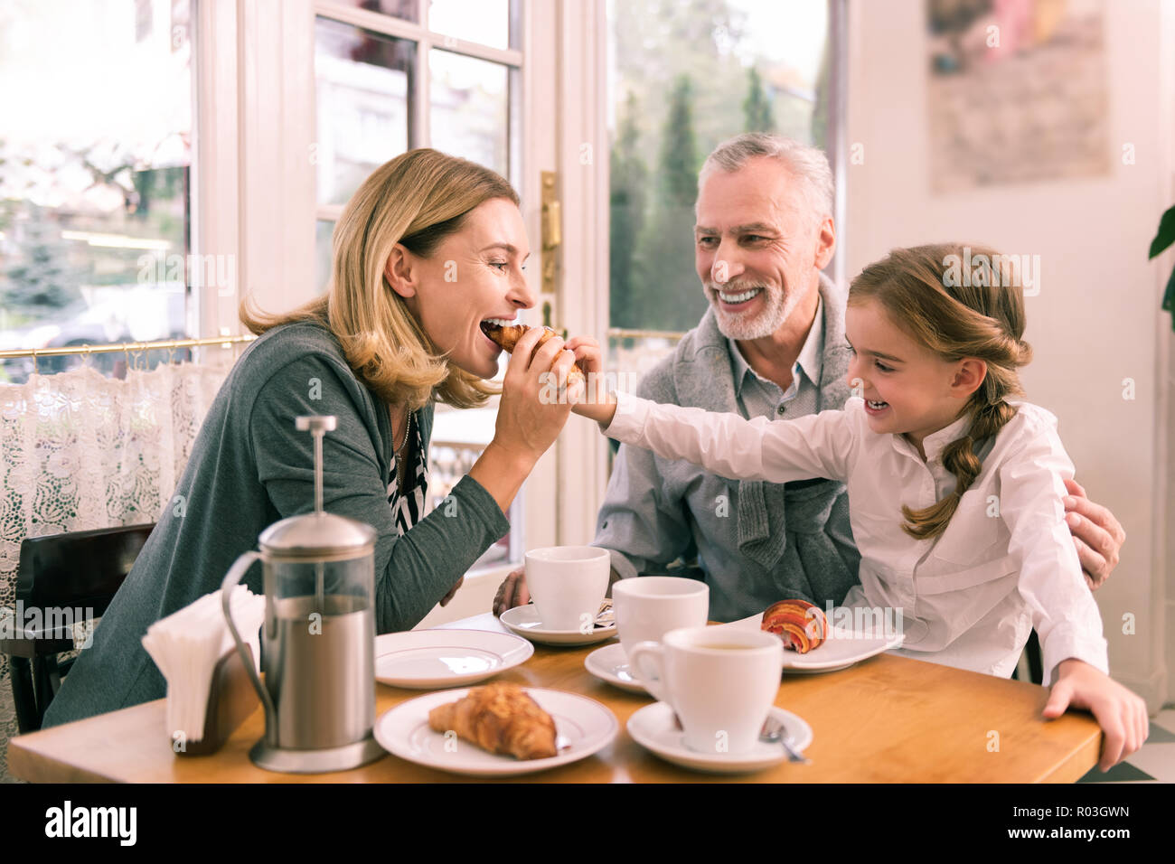 Cute kind-hearted granddaughter sharing her croissant with grandmother Stock Photo