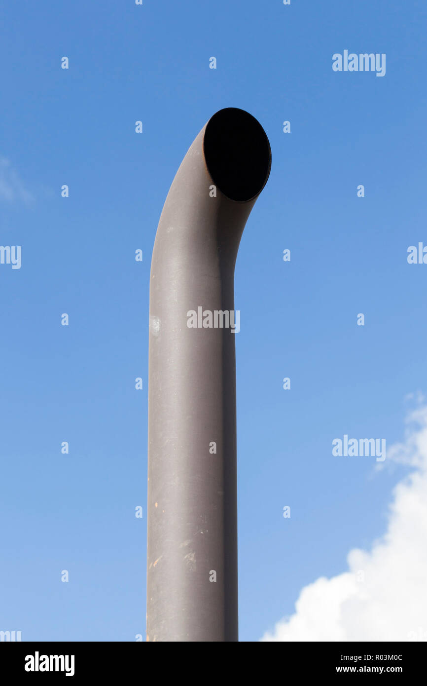 curved exhaust pipe of a tractor against the background of blue sky, dirt and soot on a metal pipe Stock Photo
