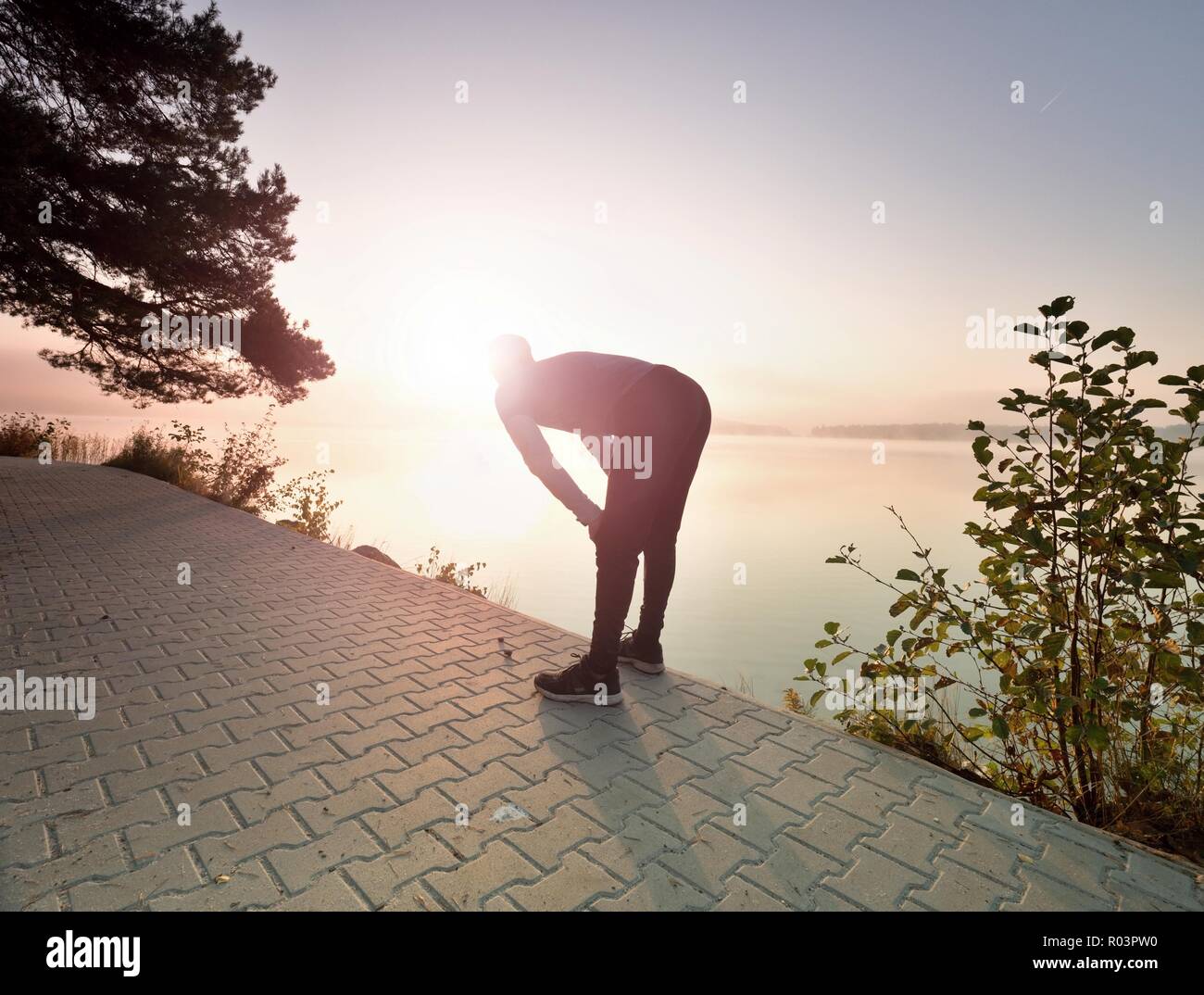 Middle aged runner stop for breath. Sportsman takes a break and looking to morning Sun above horizon Stock Photo