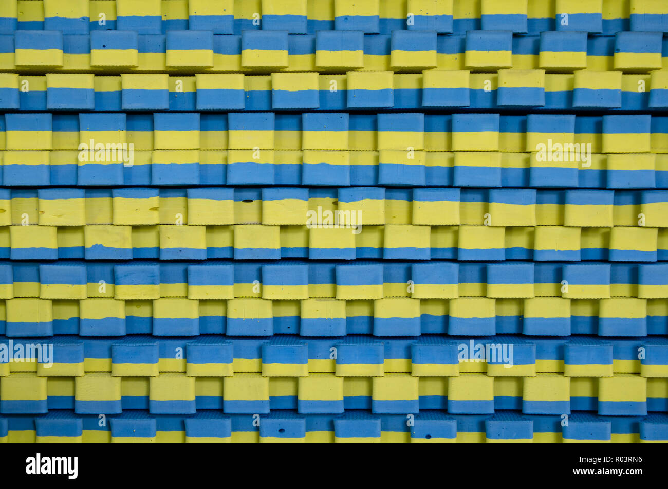 blue-yellow sports mats stacked in large stack Stock Photo