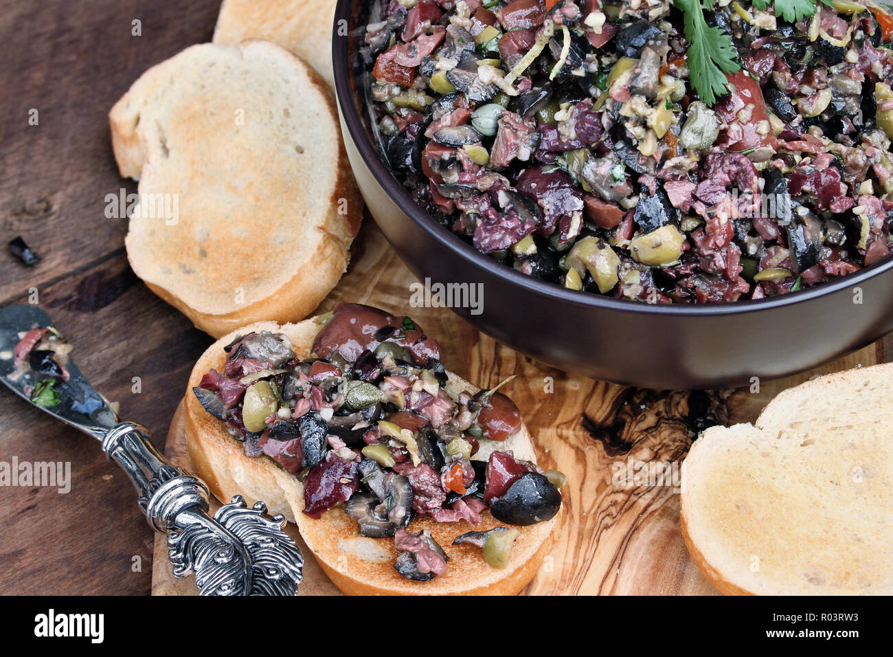 Homemade mixed Olive Tapenade made with garlic, capers, olive oil, Kalamata, black and green olives spread over toasted bread. Image shot from above. Stock Photo
