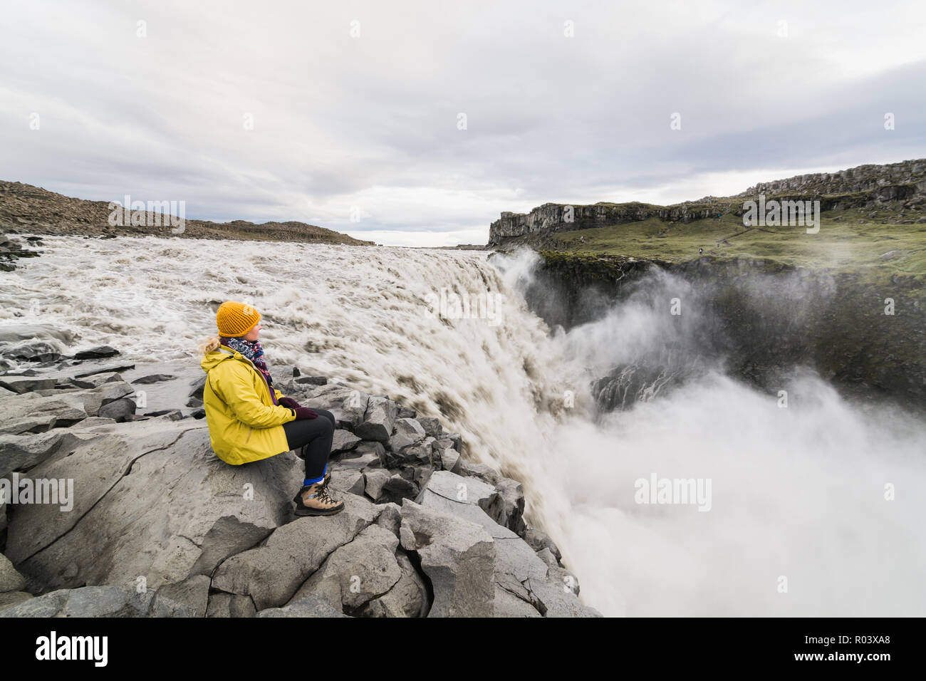 Woman in yellow raincoat sitting standing on the cliff edge next to ...
