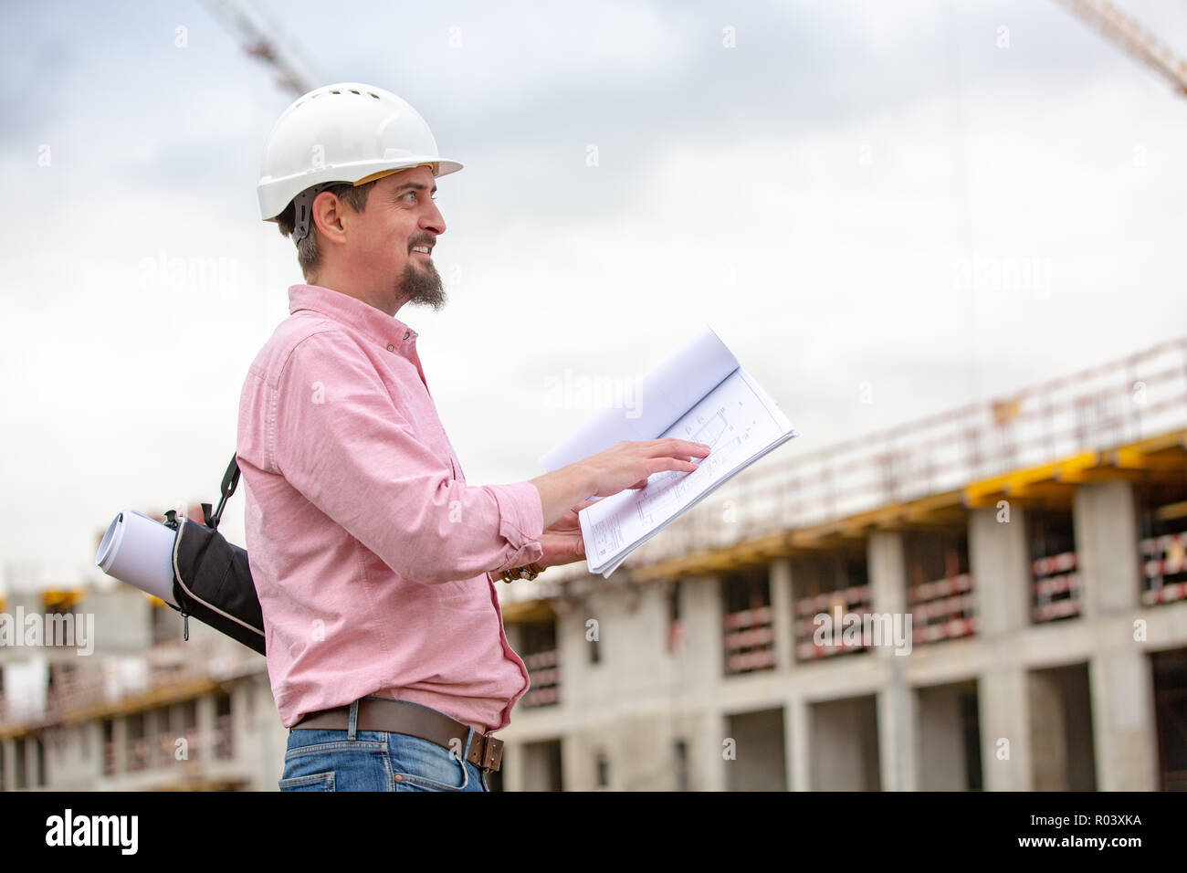 Portrait of architect at work with helmet in a construction site, reads ...