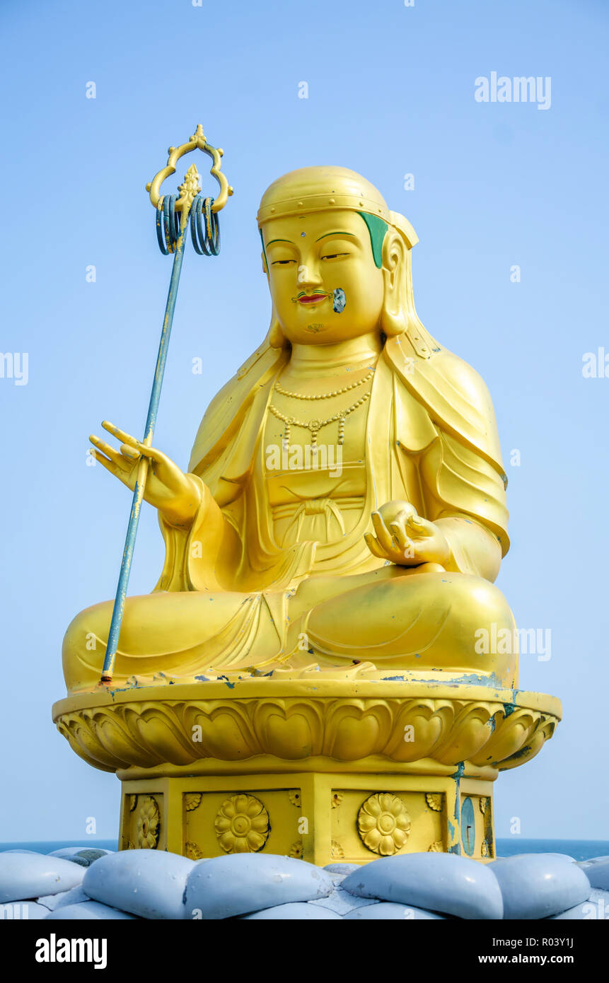 A golden statue of a Buddha sat cross legged at Haedong Yonggungsa Temple in Busan, South Korea against a blue sky. Stock Photo