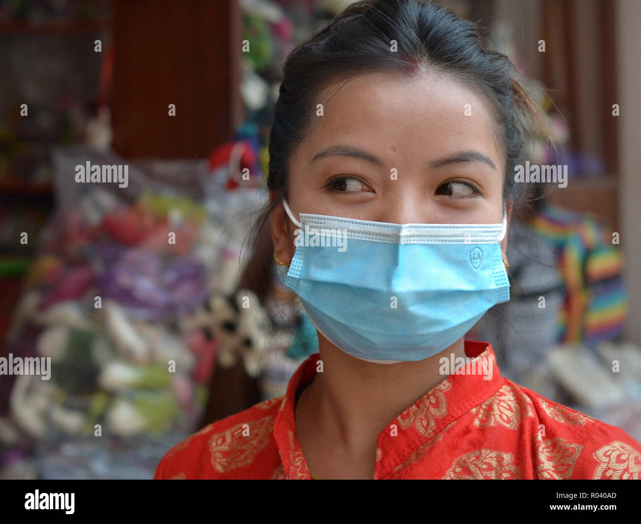 Young Nepali woman with beautiful eyes wears a light-blue disposable surgical earlobe face mask to protect herself against Kathmandu's air pollution. Stock Photo