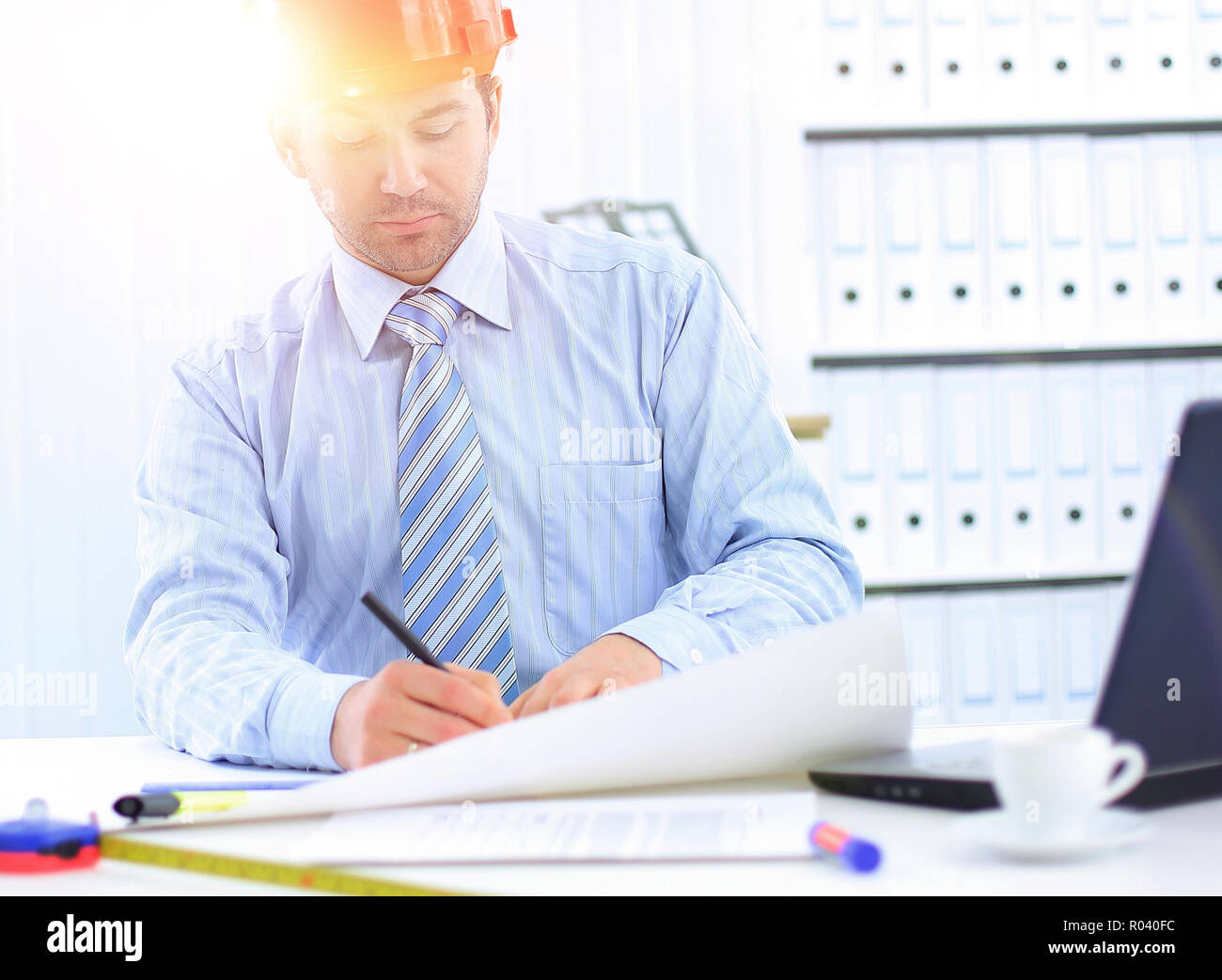 Architect looking working in office at desk. Wearing hardhat and taking notes on paper Stock Photo