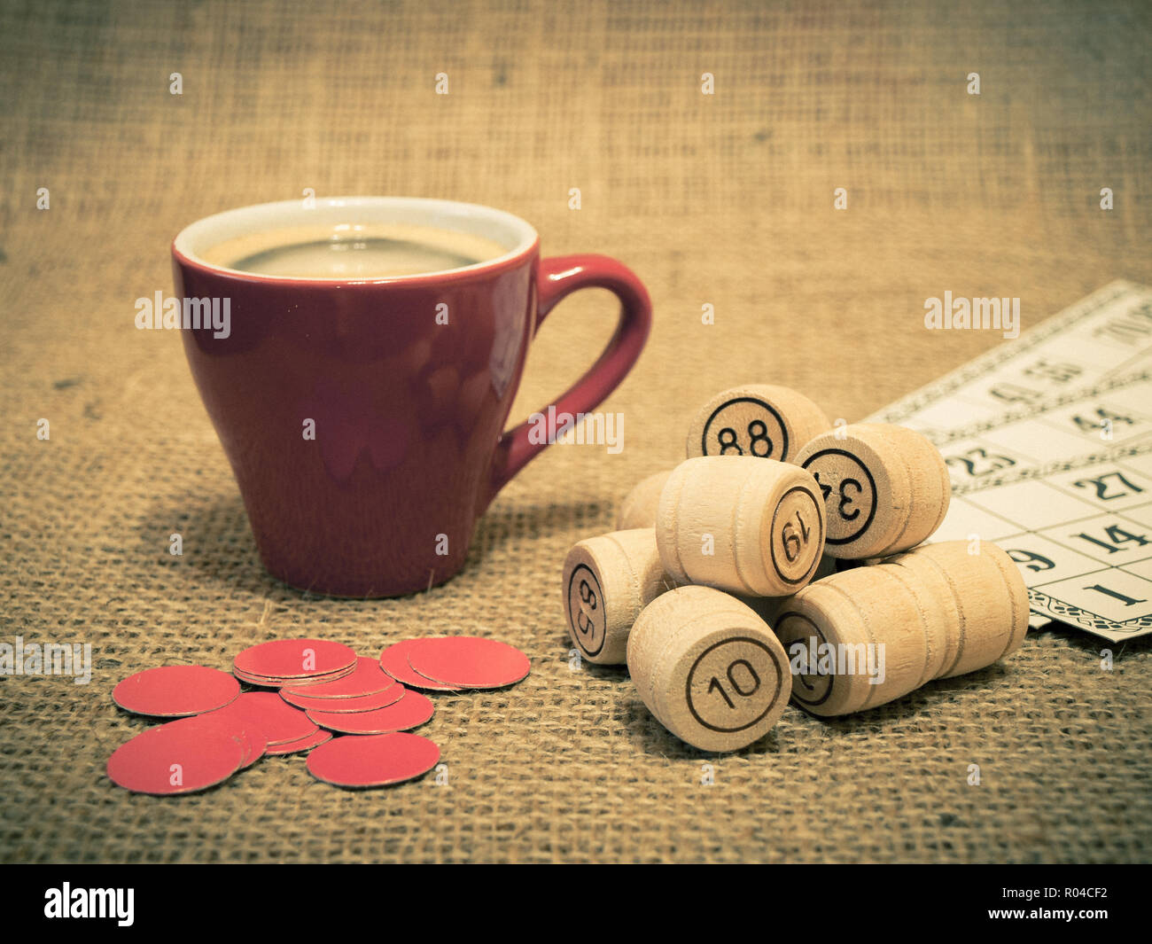 Board game lotto. Wooden lotto barrels, game cards, red chips for a game in lotto and cup of coffee on sackcloth. Color toning effect. Stock Photo