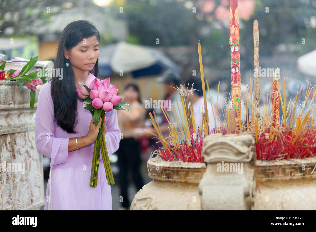 Elegant Vietnamese girl praying and offering fresh lotus flowers at a
