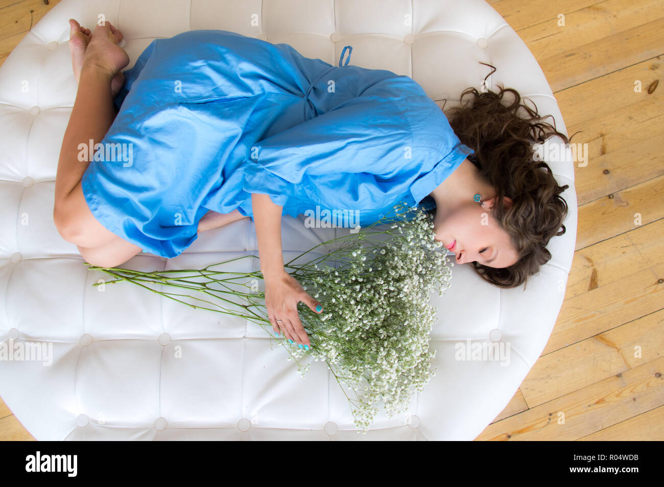 Pregnant woman in blue dress with closed eyes lies on round sofa with bouquet of flowers Stock Photo