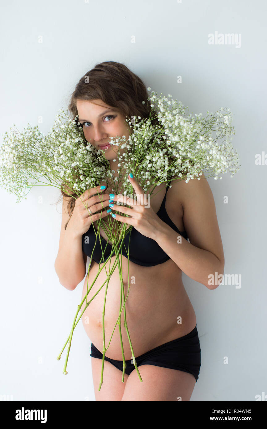 Pregnant woman with bouquet of flowers in hands , white wall on background Stock Photo