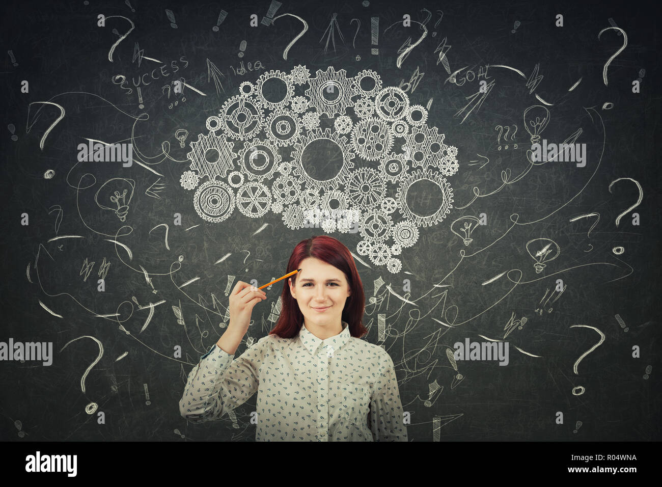 Puzzled businesswoman having questions in front of a blackboard. Big chalk drawn gear brain above head, positive thinking mess as thoughts. Concept fo Stock Photo