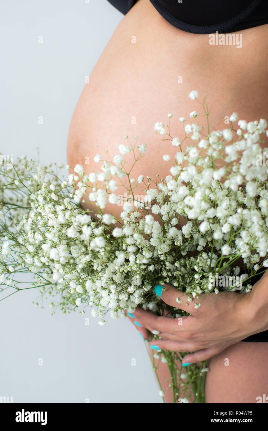 Tummy of pregnant woman with bouquet of flowers in hands , white wall