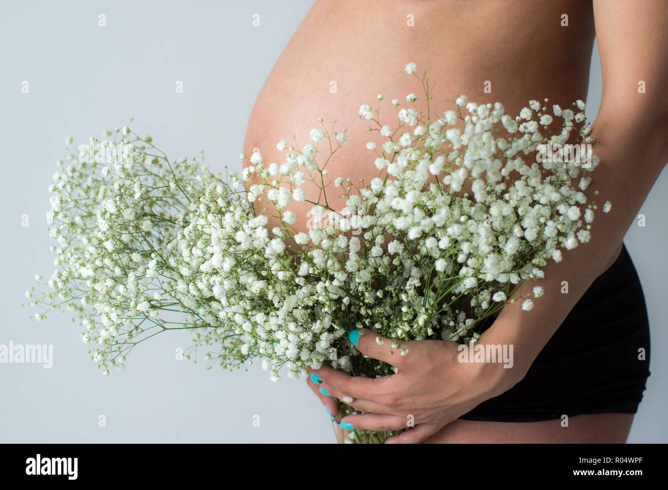 Tummy of pregnant woman with bouquet of flowers in hands , white wall on background Stock Photo