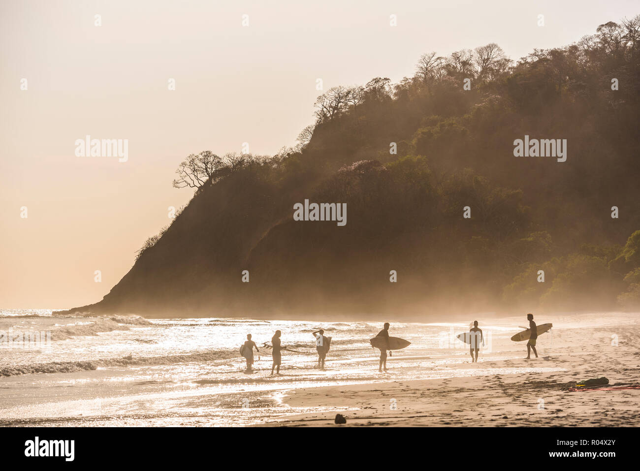 Surfers surfing on a beach at sunset, Nosara, Guanacaste Province, Pacific Coast, Costa Rica, Central America Stock Photo