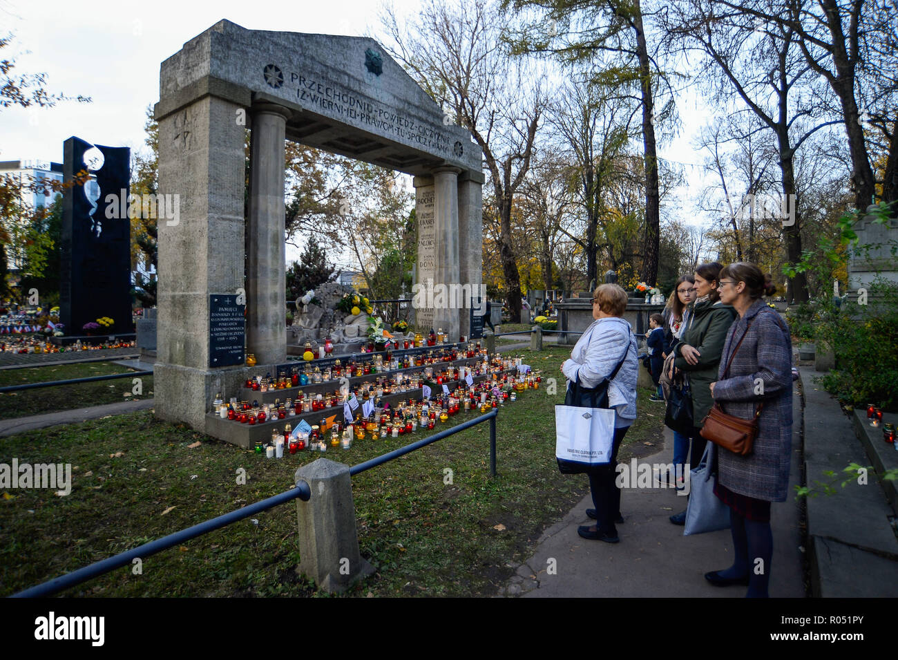 Krakow, Poland. 1st Nov, 2018. People are seen standing next to a grave with candles at the Rakowicki Cemetery during the celebrations.All Saints Day, also known as The Day of the Dead, is a Roman Catholic day of remembrance of friends and loved ones who have passed away. Credit: Omar Marques/SOPA Images/ZUMA Wire/Alamy Live News Stock Photo