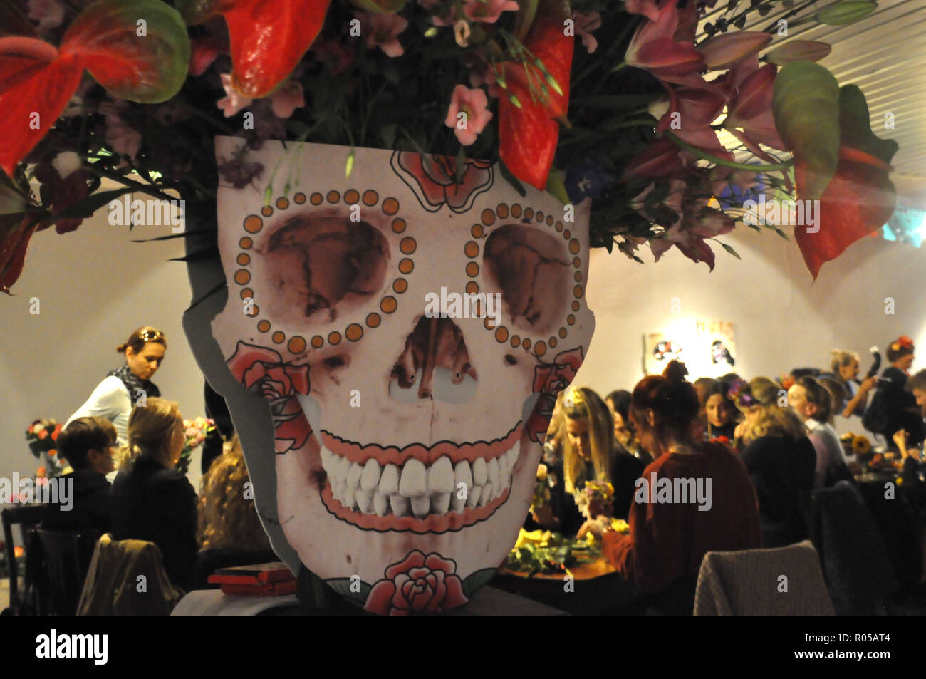 Hamburg, Germany. 02nd Nov, 2018. A cardboard skull stands in a gallery on St. Pauli on the occasion of the Mexican holiday 'Dia de los muertos'. In the background, visitors weave wreaths of flowers. (to dpa: 'Hundreds of hamburgers celebrate Mexican 'Day of the Dead'') Credit: Hannah Wagner/dpa/Alamy Live News Stock Photo