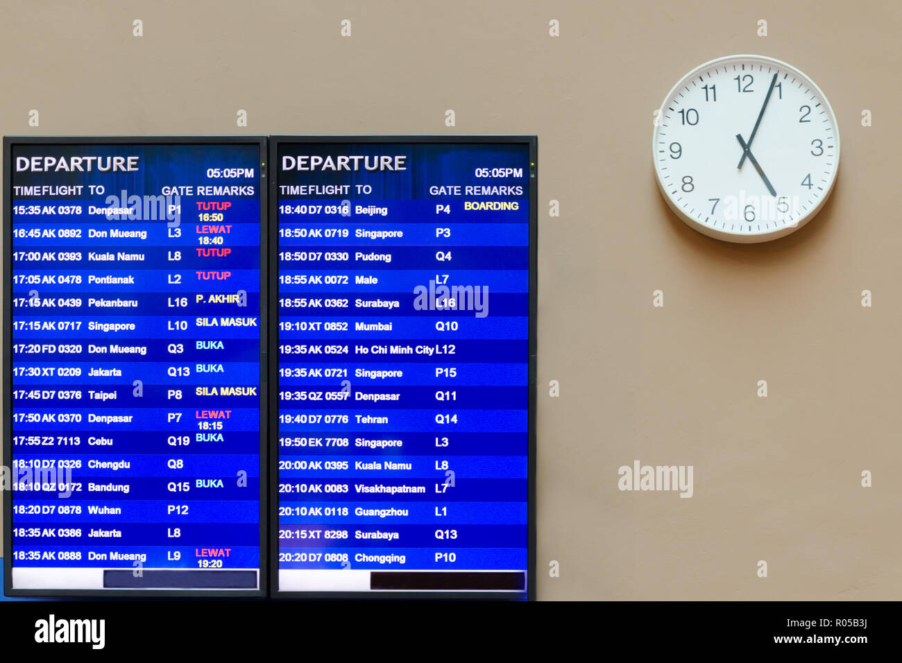 Airport information board, near the clock with hands that shows four minutes past five, flight schedule. Malaysia, Kuala Lumpur, KLIA 2. Stock Photo