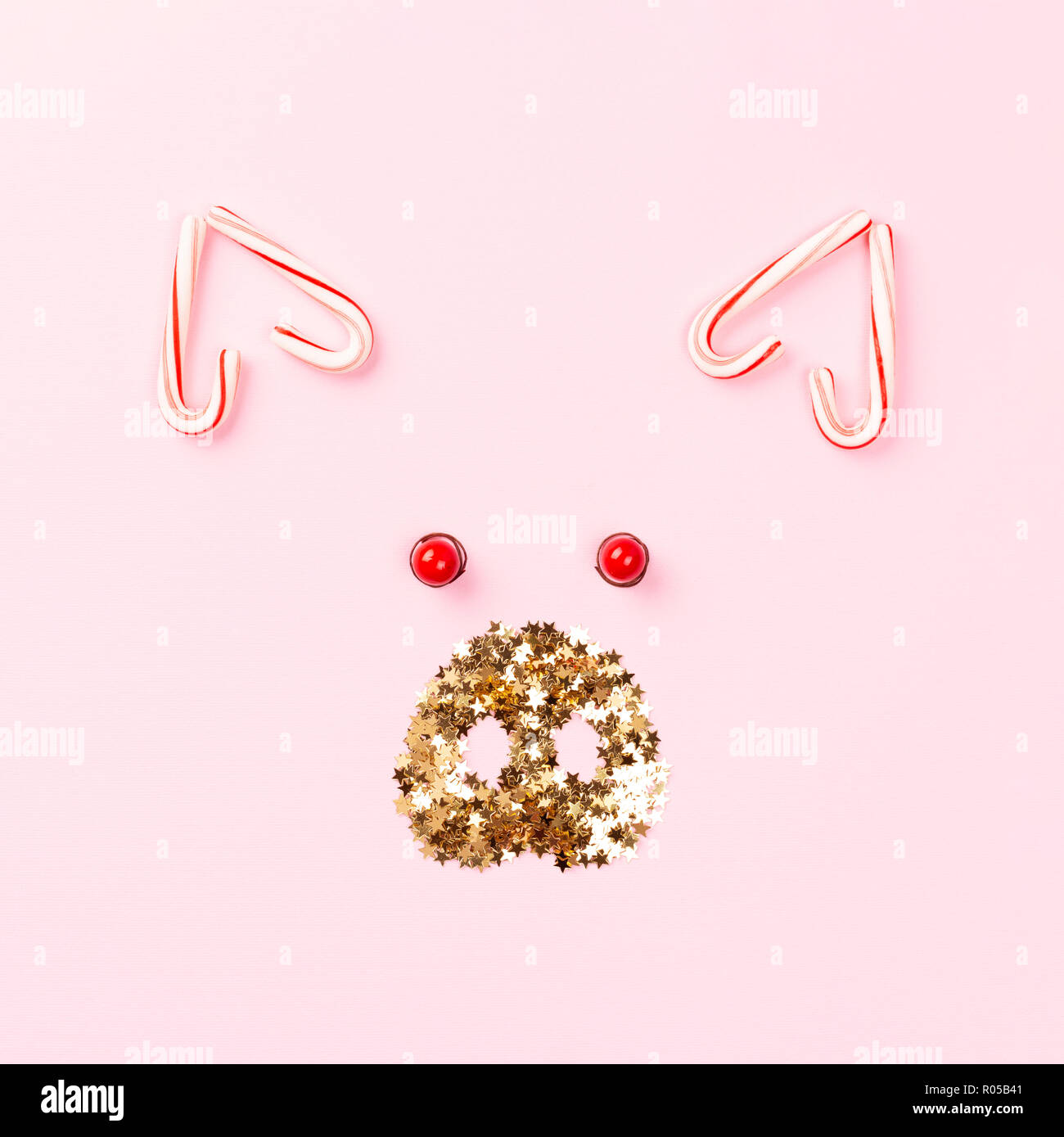 Christmas pig concept made of candy cane lollipops and golden confetti on pink background. Stock Photo
