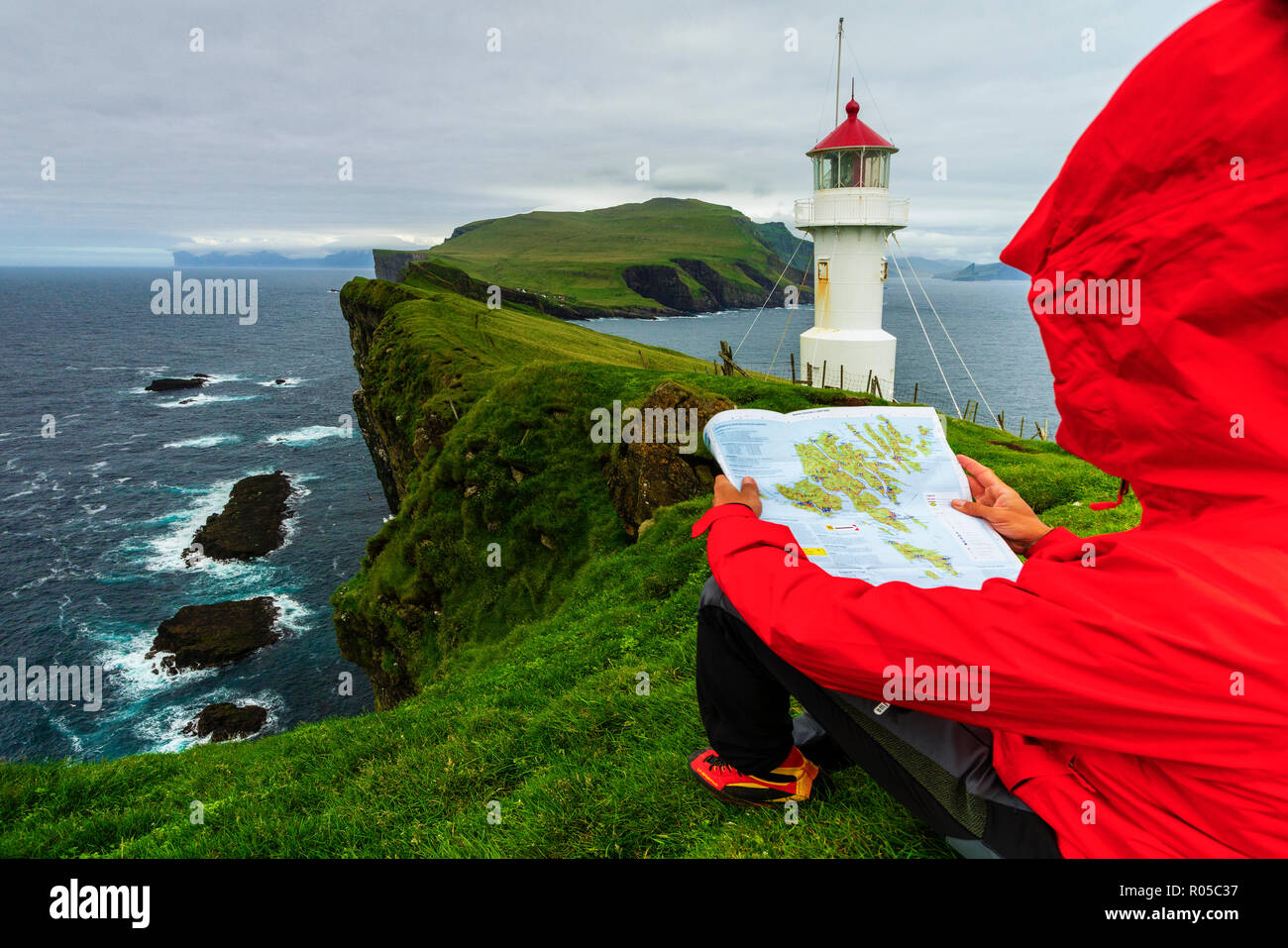 Hiker on cliffs looks at the map next to lighthouse, Mykines island, Faroe Islands, Denmark Stock Photo