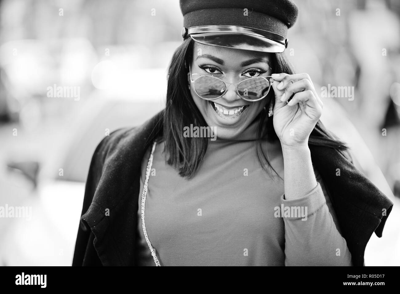 African american fashion girl in coat, newsboy cap and sunglasses posed at street against white business car. Stock Photo