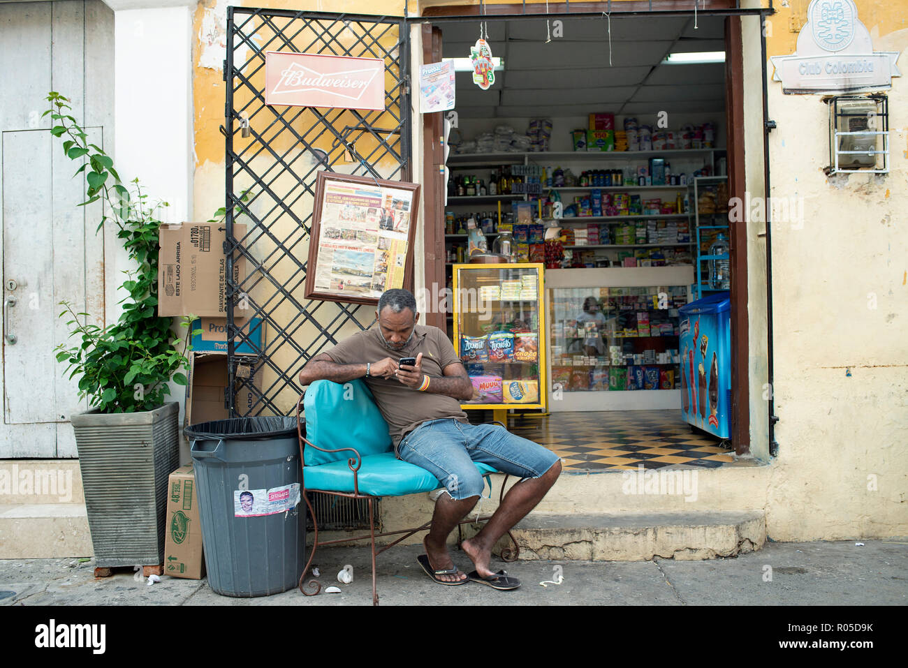 Unidentified Colombian man sits outside his shop in Getsemani, checking his mobile phone. Cartagena de Indias, Colombia. Oct 2018 Stock Photo