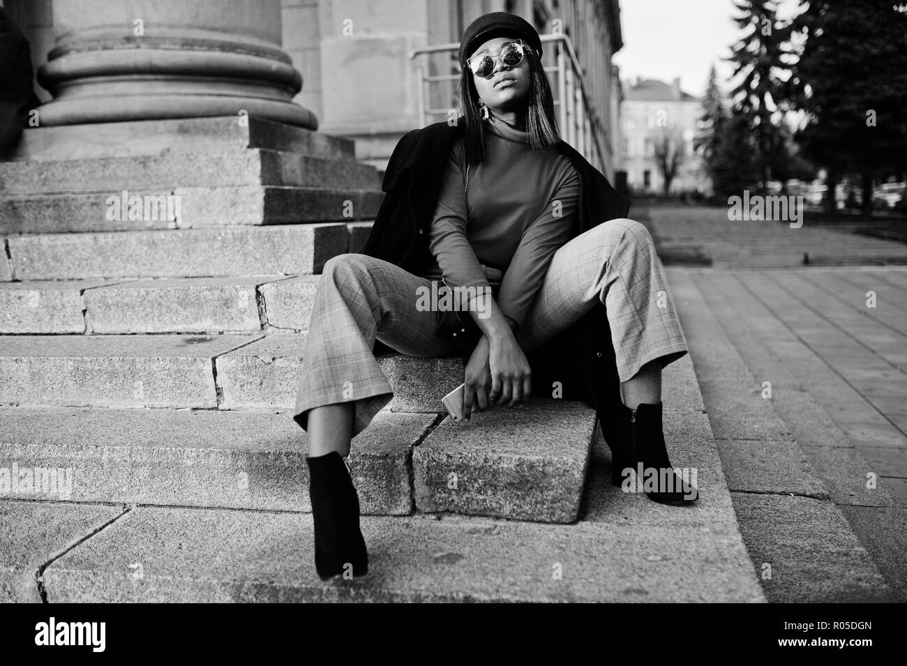 African american fashion girl in coat and newsboy cap, sunglasses posed at street. Stock Photo