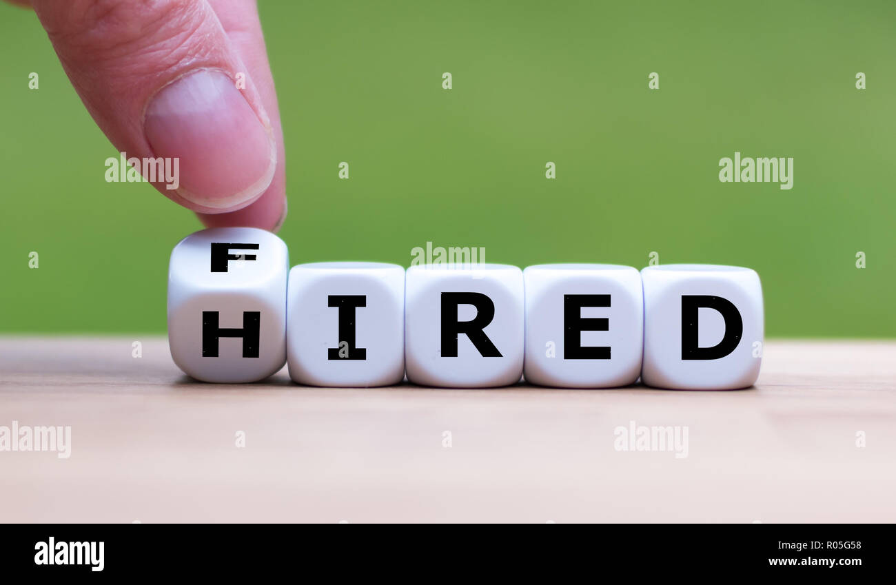 Hand is turning a dice and changes the word 'fired' to 'hired' Stock Photo