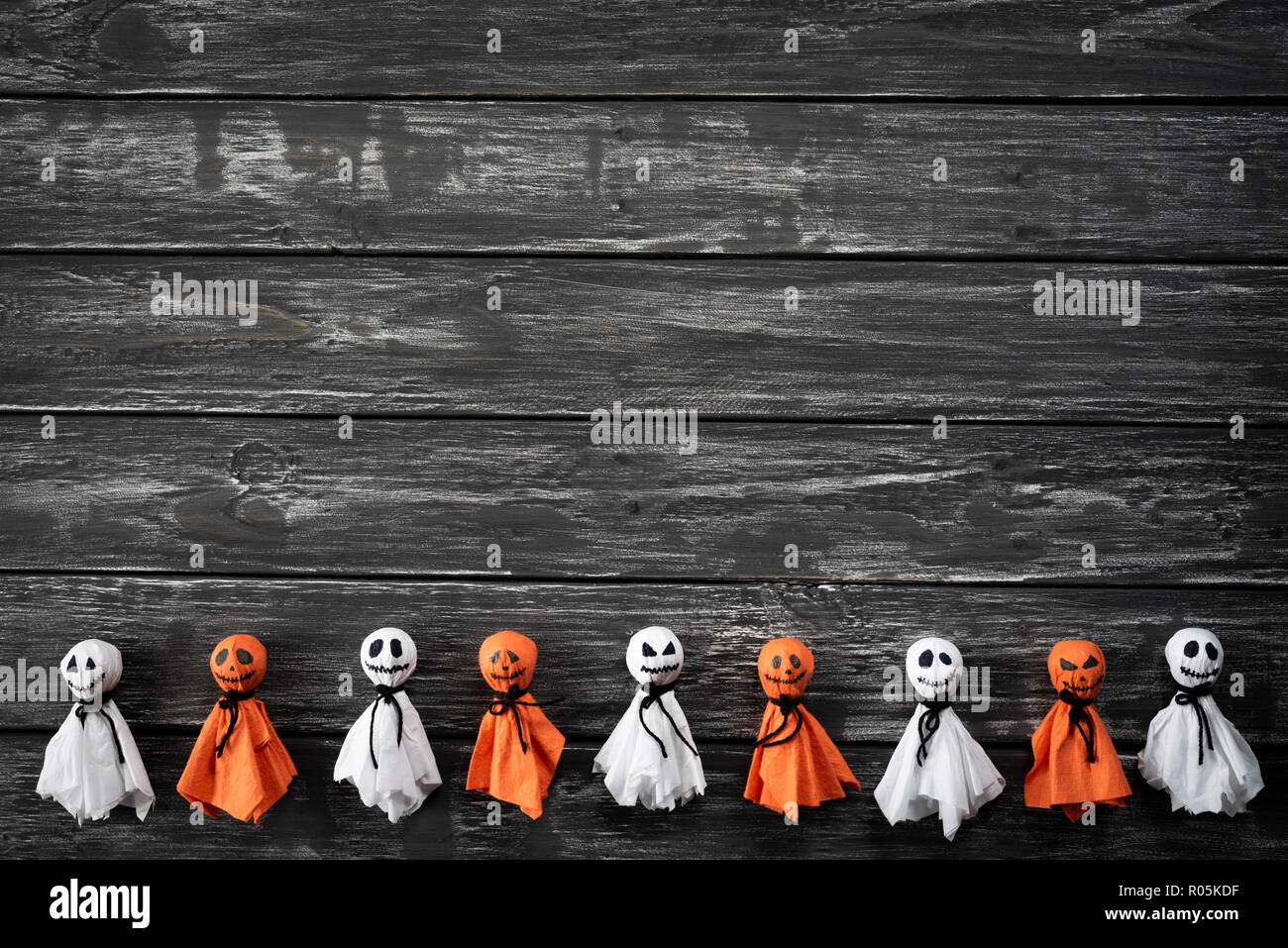 Top view of Halloween crafts, white and orange paper ghost on black and ...