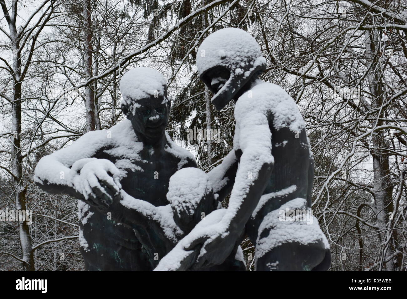 A bronze statue covered in snow at the War Cemetery in Reimsbach depicts two men carrying a deadly victim as a symbol of the helplessness of man . Stock Photo