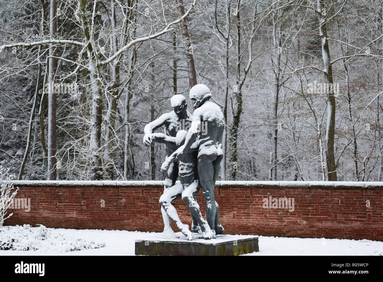 A bronze statue covered in snow at the War Cemetery in Reimsbach depicts two men carrying a deadly victim as a symbol of the helplessness of man . Stock Photo