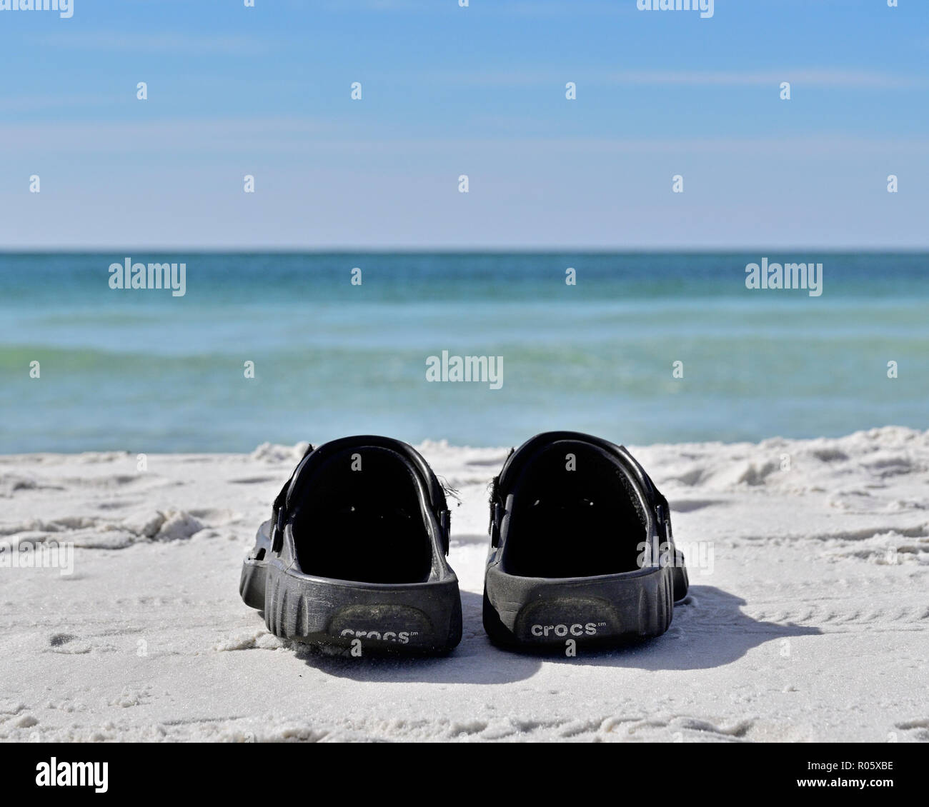 Pair of Crocks beach shoes or sandals on white Florida panhandle Gulf coast beach sand facing the Gulf of Mexico at Deer Lake State Park, Florida USA. Stock Photo