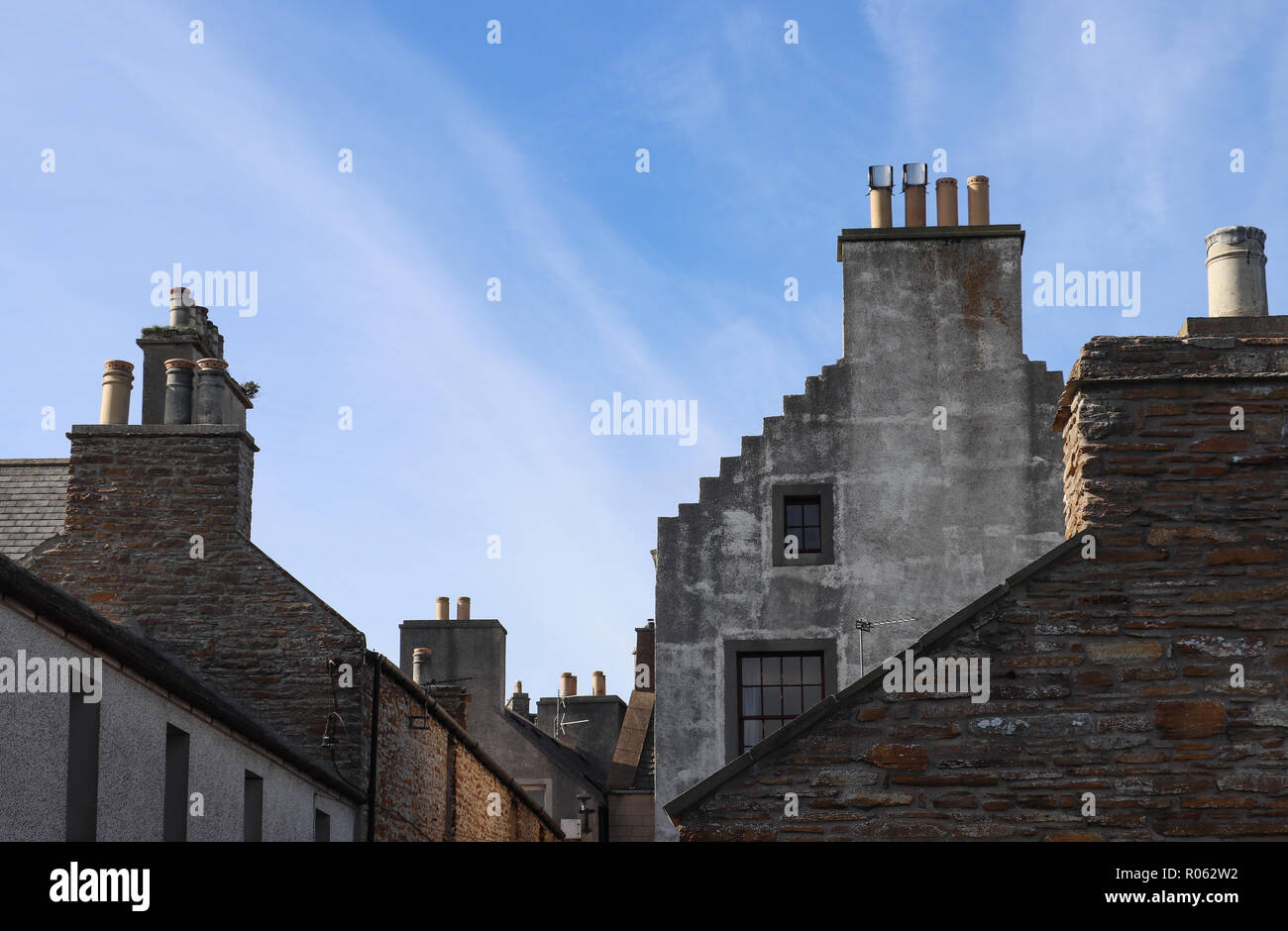 Several 18-19th Century buildings with stepped gable ends and many chimneys in Stromness, Scotland, seen against a blue sky with lots of copy space. Stock Photo