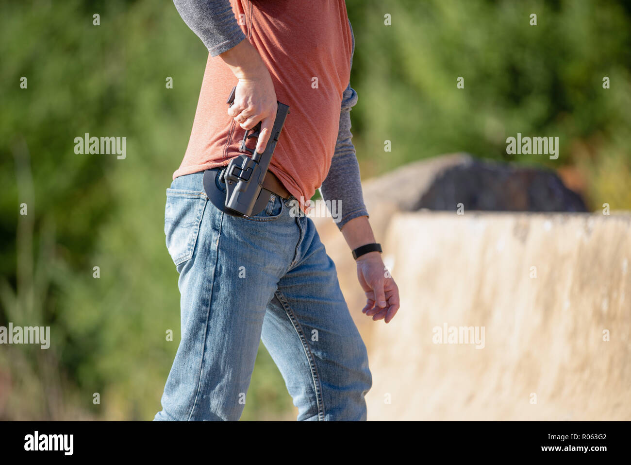 Adult male person in jeans and hoodie removing black handgun from a gun