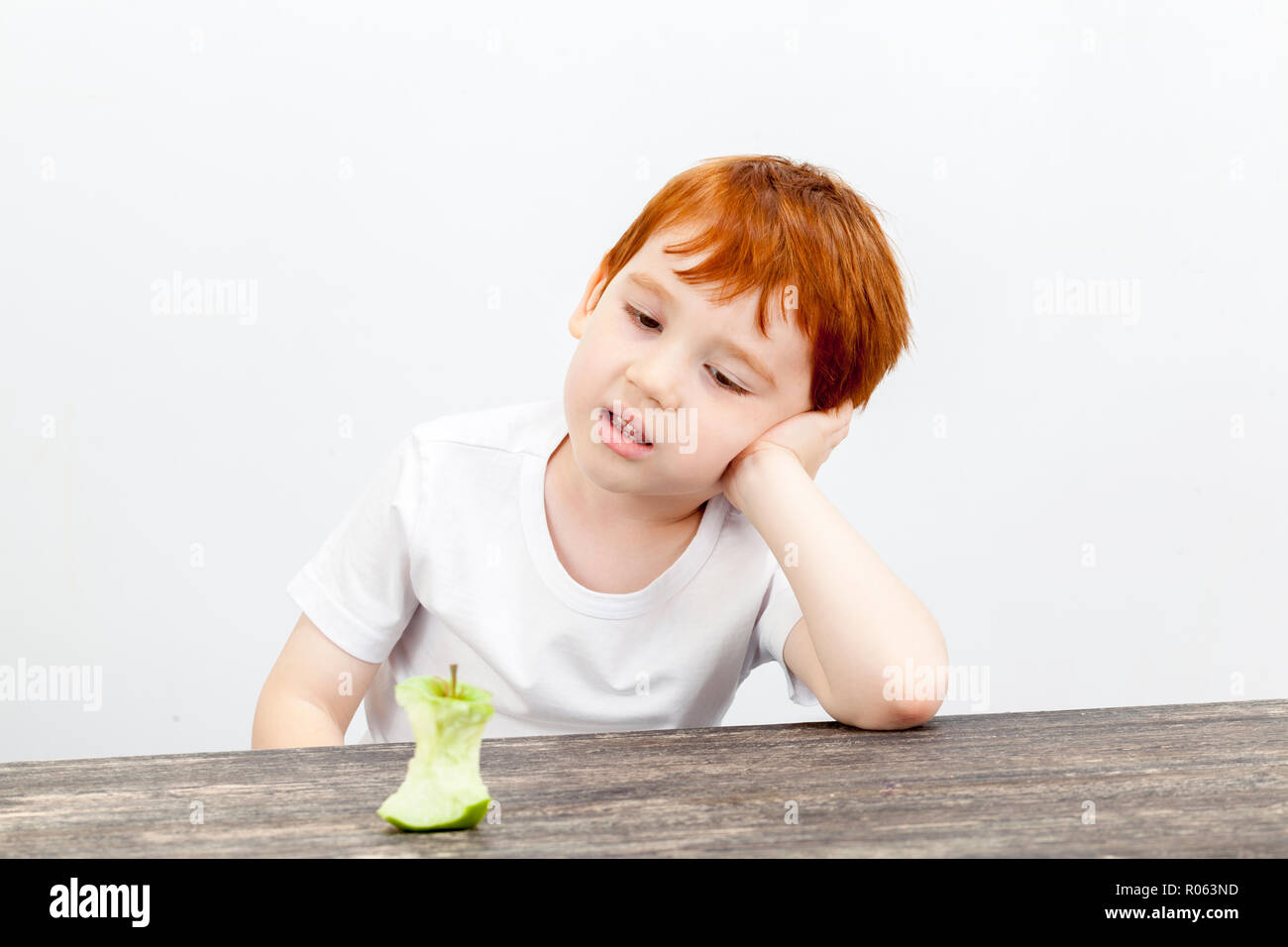 portrait of a boy with red hair and freckles at a kitchen table, looking at a stub of a large apple eaten, little used post-processing a portrait, a b Stock Photo