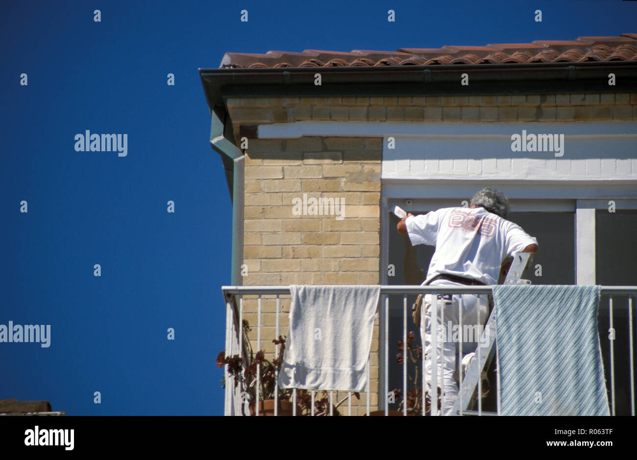 House painter at work painting the window trames of a suburban brick home in Sydney, New South Wales, Australia Stock Photo