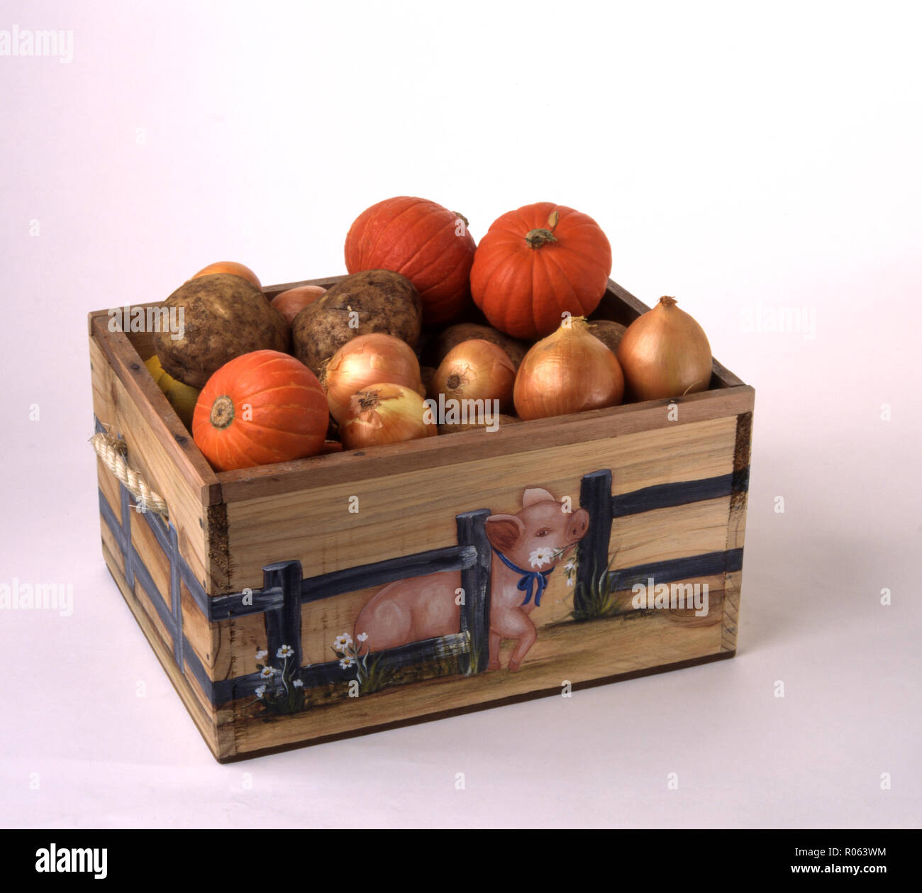 Hand painted decorated with pink pig wooden vegetable box containing harvested pumpkins, onions and potatoes Stock Photo