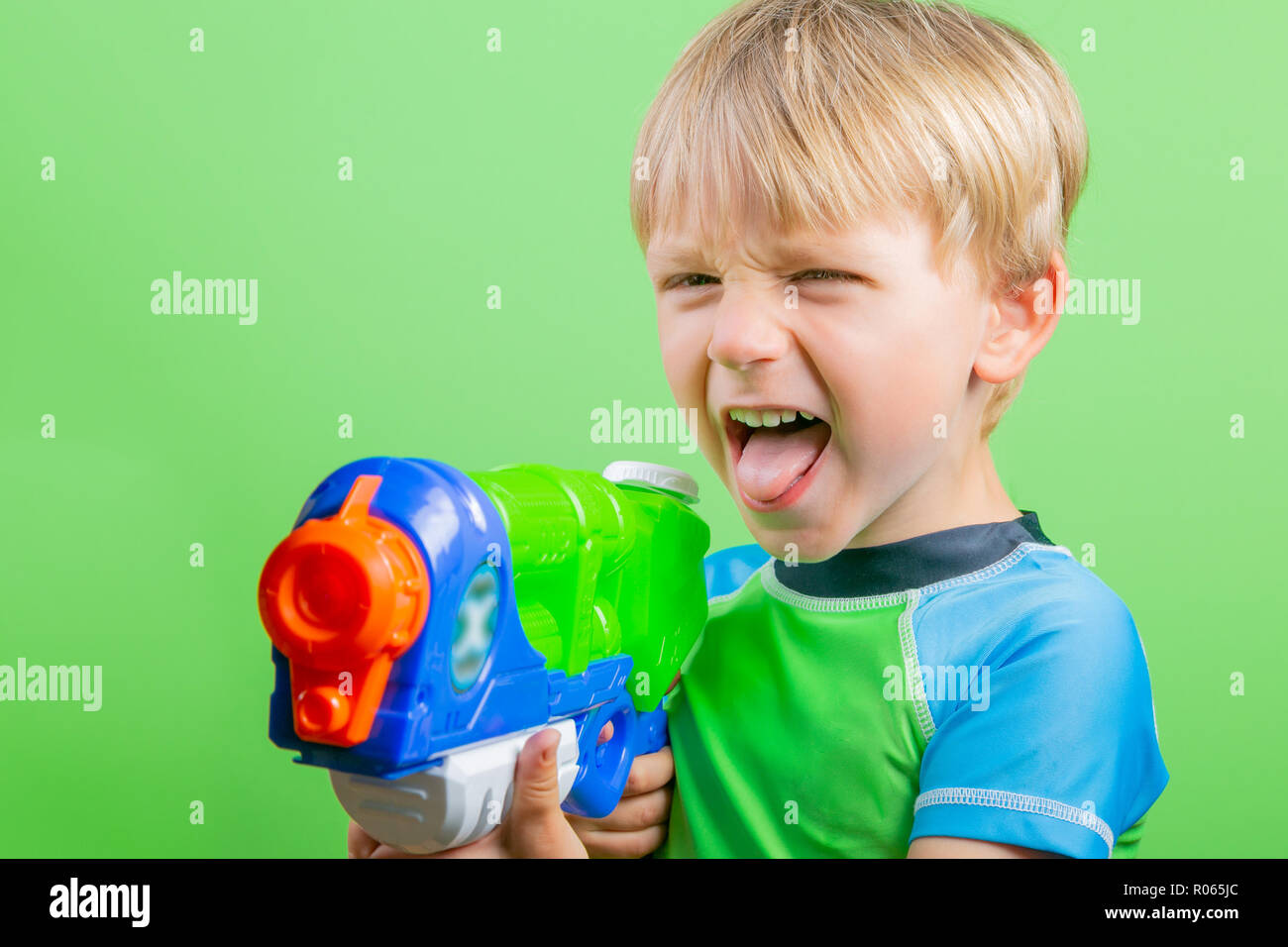 Boy holds water gun and looks at camera in front of bright green