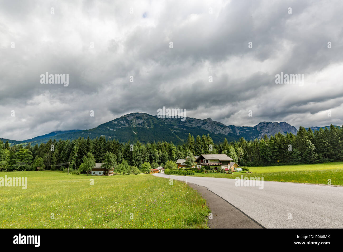 Alps in Austria. Wooden house before mountains green field and road through green pine forest Stock Photo