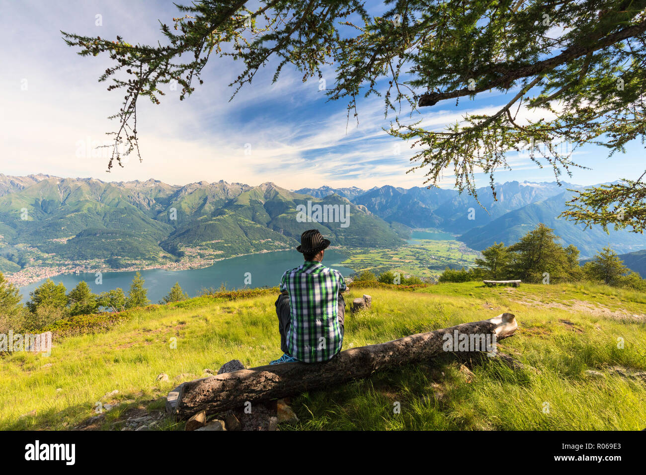 Man sitting on tree trunk looks towards Lake Como and Alto Lario, Monte Legnoncino, Lecco province, Lombardy, Italy, Europe Stock Photo