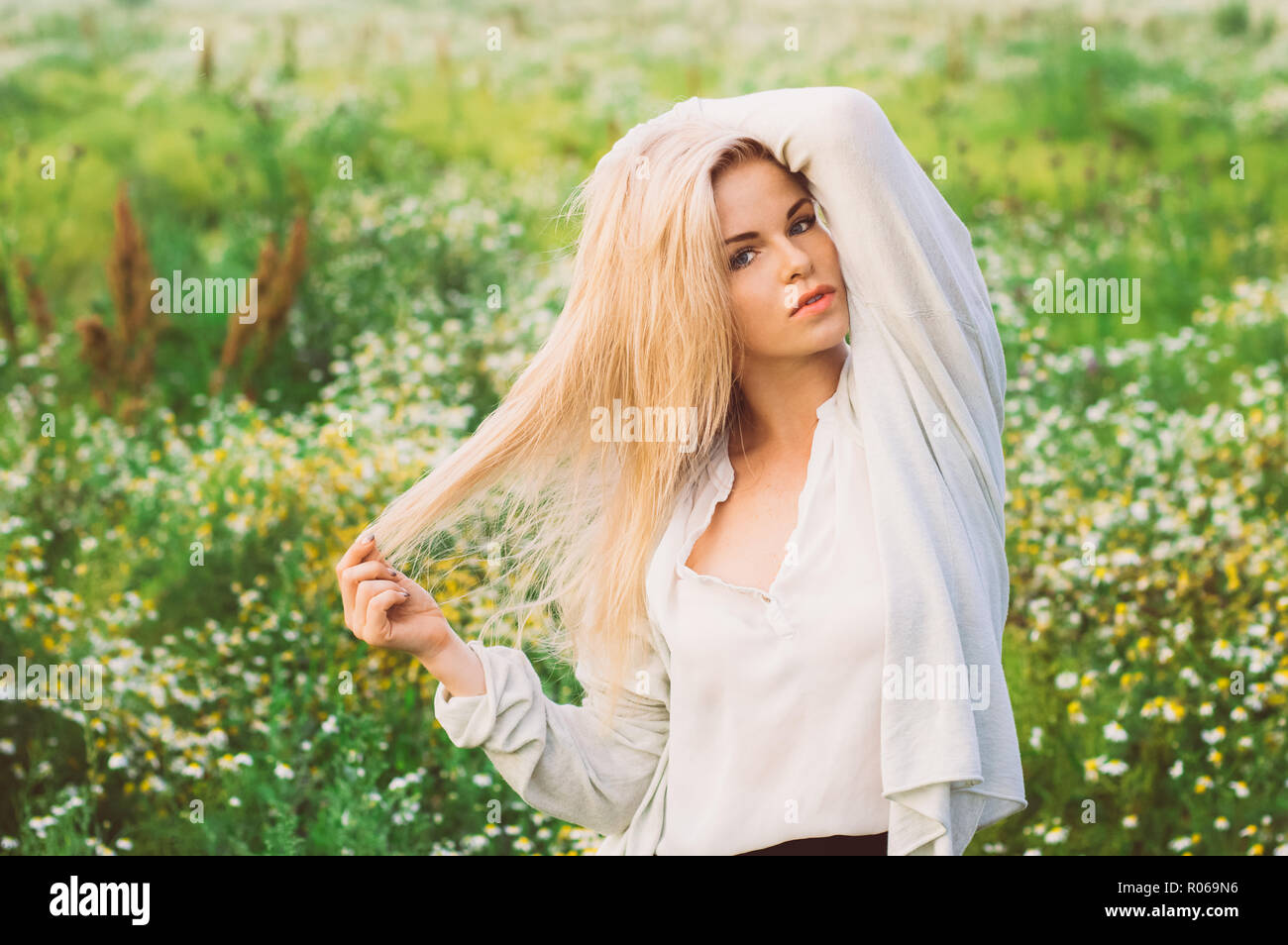 Portrait of young girl staying in chamomile field with hands on head ...