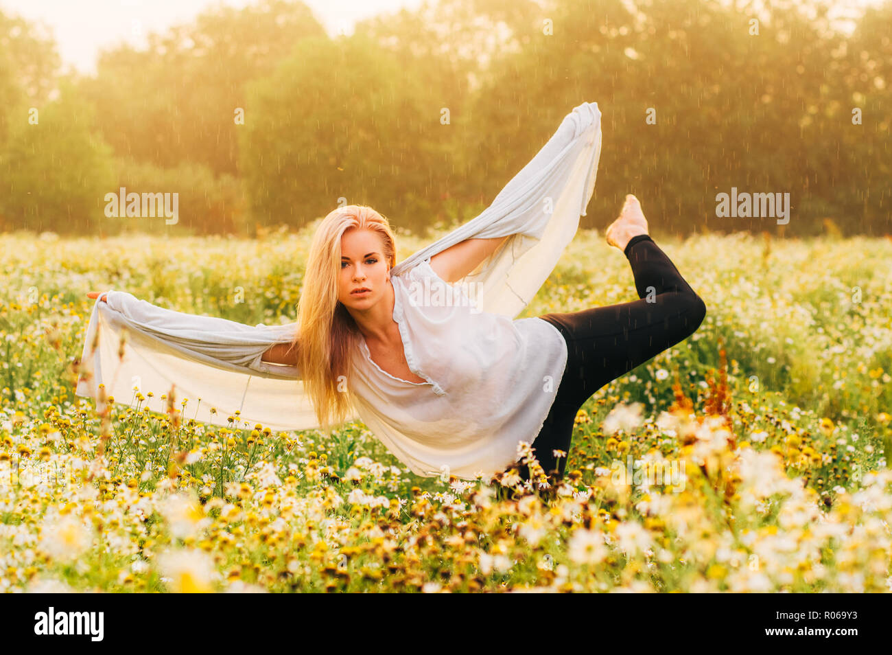 Portrait of young girl dancing in chamomile field under the rain ...