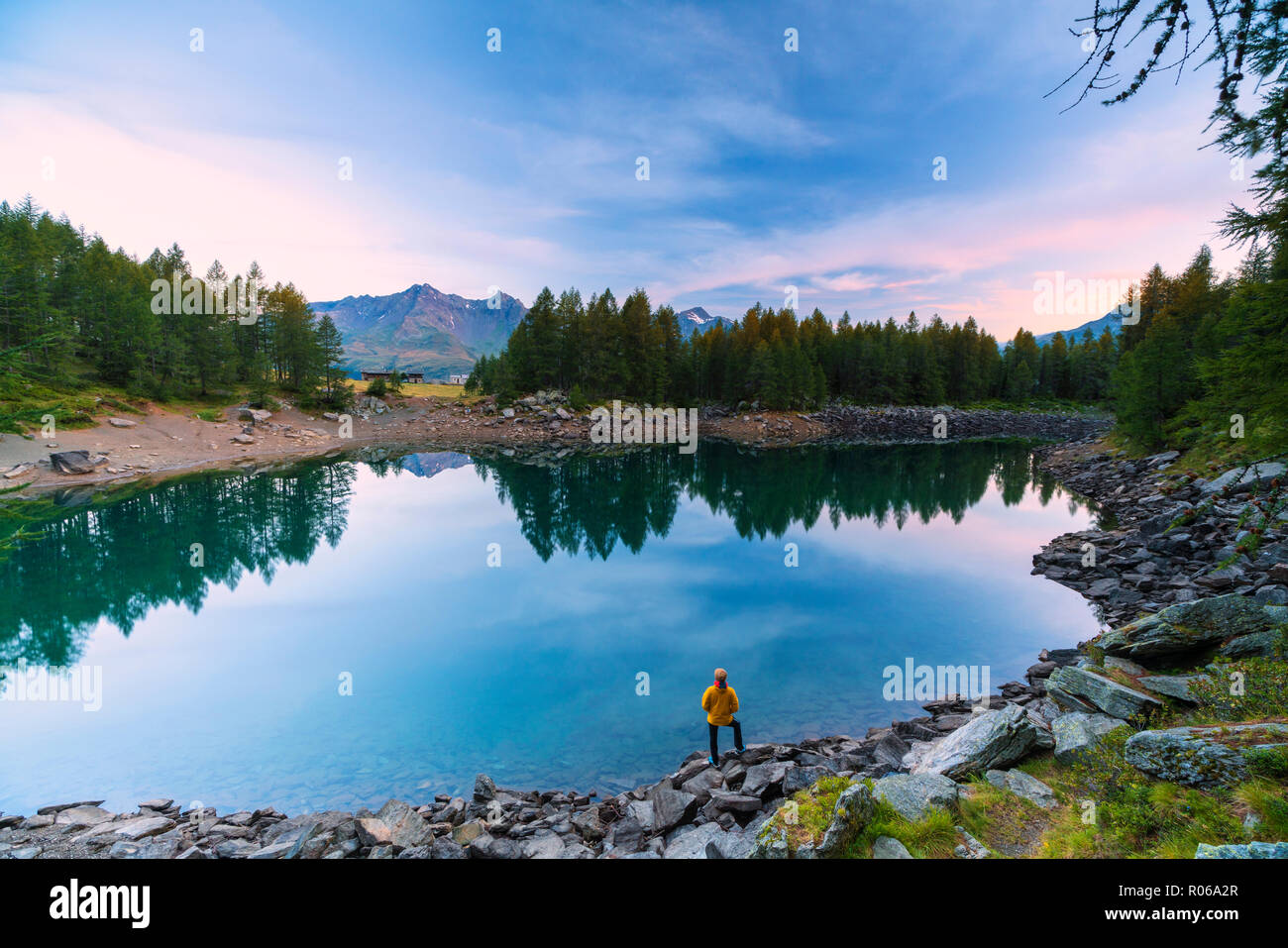 Hiker admires sunrise on lakeshore, Lago Azzurro, Spluga Valley, Sondrio province, Valtellina, Lombardy, Italy, Europe Stock Photo