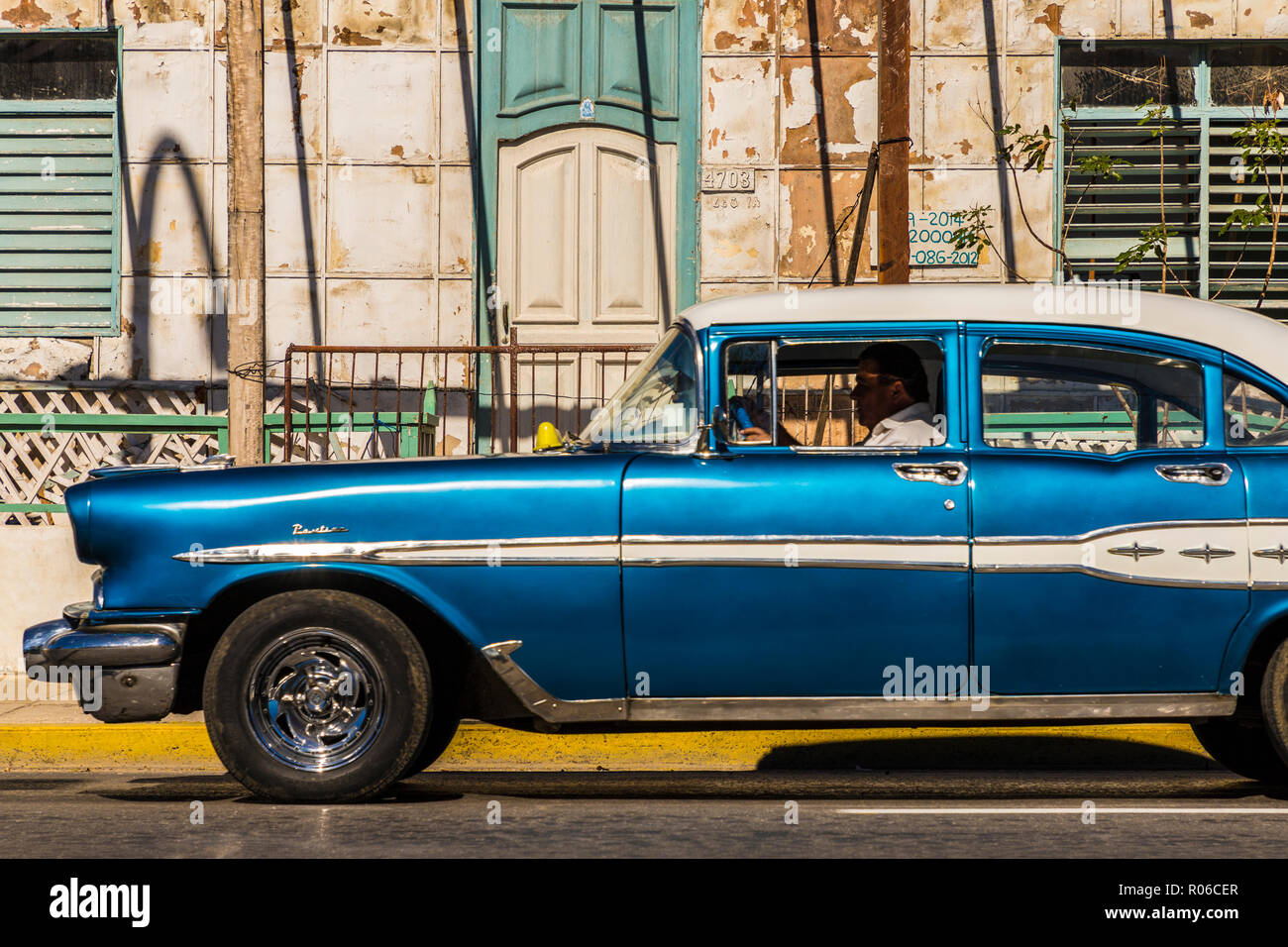 A classic American car driving past an old building in Varadero, Cuba, West Indies, Caribbean, Central America Stock Photo