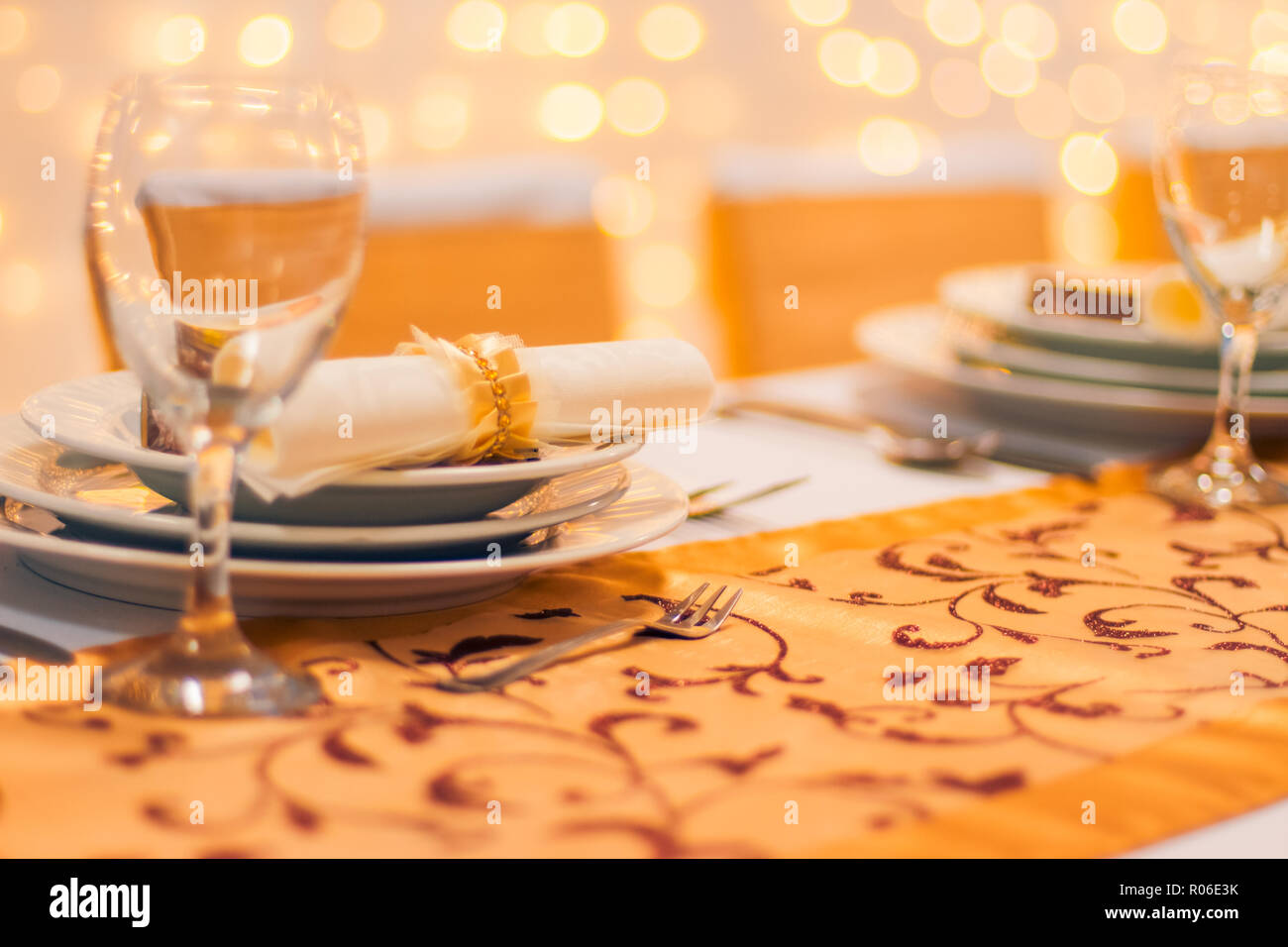 Plate at the wedding table, wine glass and blurred golden bokeh lights. Amazing wedding concept background. Luxury and elegant table setup for wedding Stock Photo