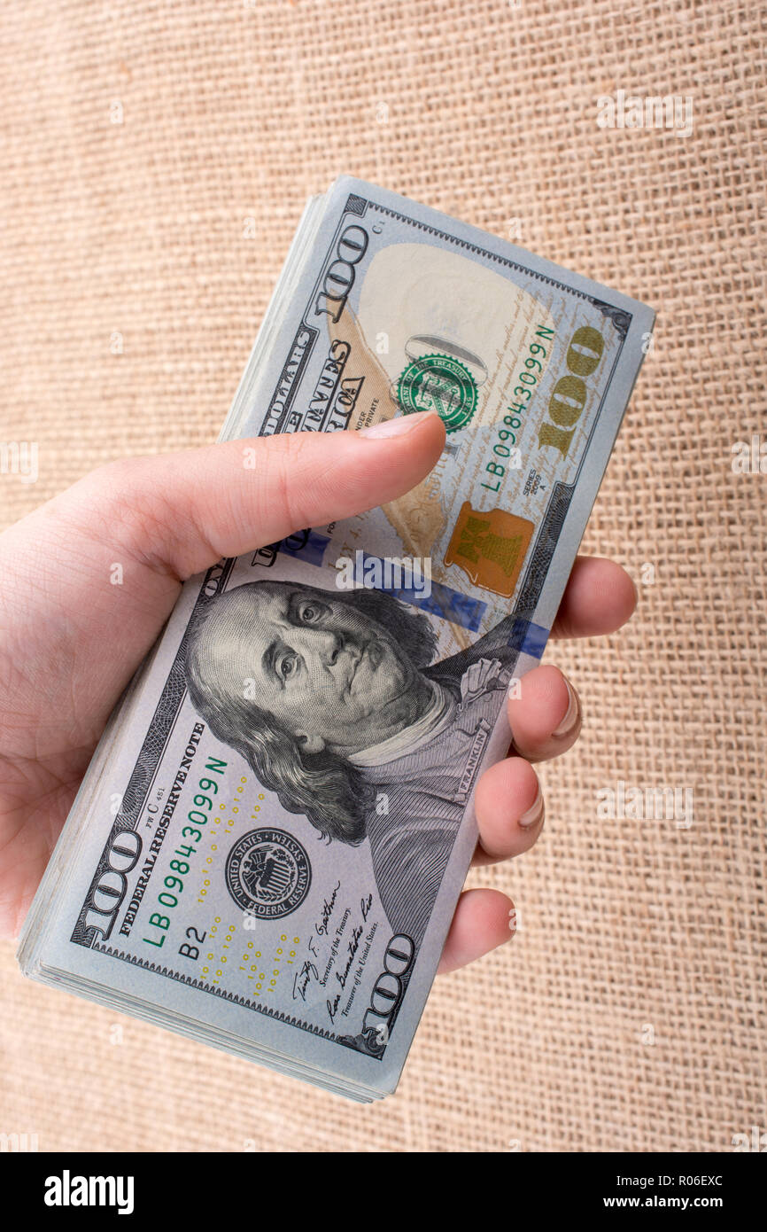 Hand holding banknote bundle of US dollar on a linen canvas background ...
