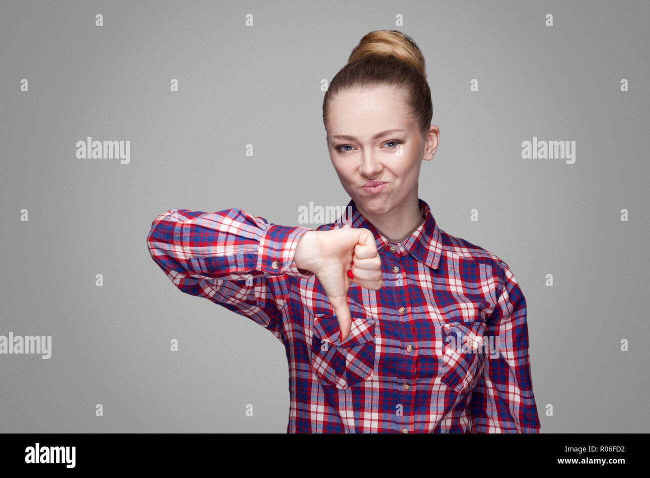 Unhappy sad girl with pink checkered shirt, collected bun hairstyle and makeup standing and looking at camera with unsatisfied face and thumbs down. i Stock Photo - Alamy Unhappy sad girl with pink checkered shirt, collected bun hairstyle and makeup standing and looking at camera with unsatisfied face and thumbs down. i Stock Photo - Alamy
