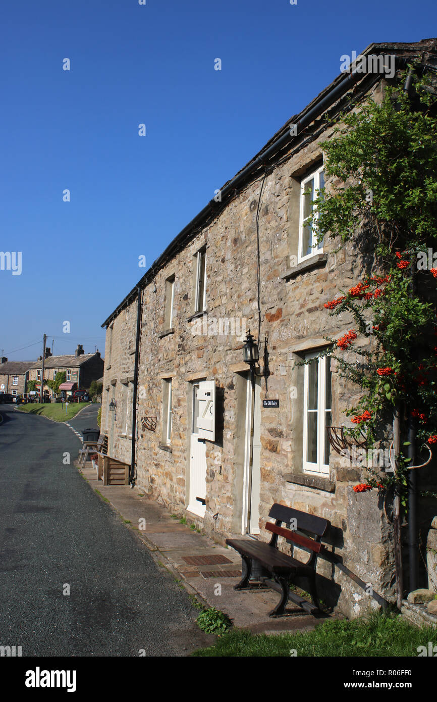 Holiday cottages with wooden seats outside on roadside on side of main road through Muker in Swaledale, Yorkshire Dales, North Yorkshire, UK. Stock Photo