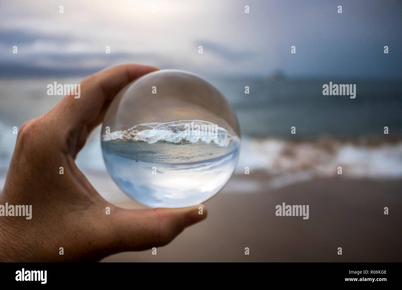 Stormy surf breaking on sand captured in glass ball reflection held in fingertips Stock Photo