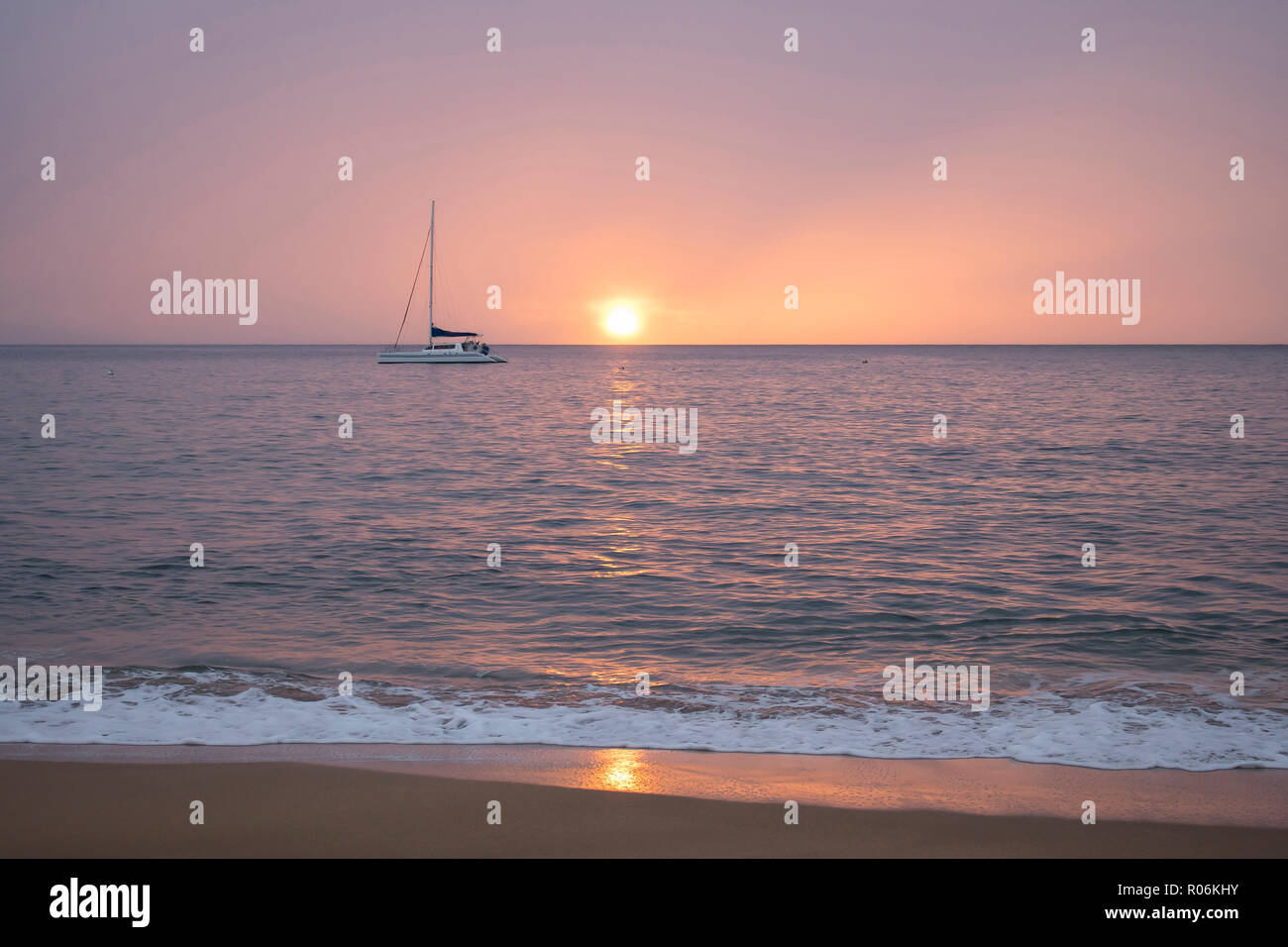 Muted Pink Sunset Seascape with Boat and Sun on Horizon and Light Reflecting on Ocean Surface Stock Photo