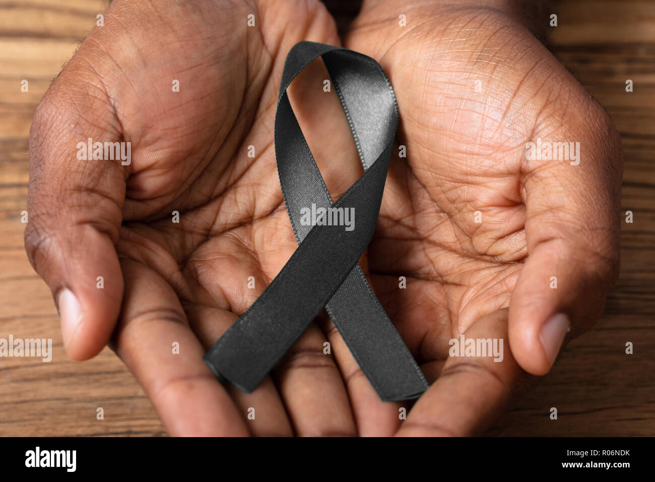 Person's Hand Holding Ribbon To Support Melanoma Skin Cancer Awareness Stock Photo